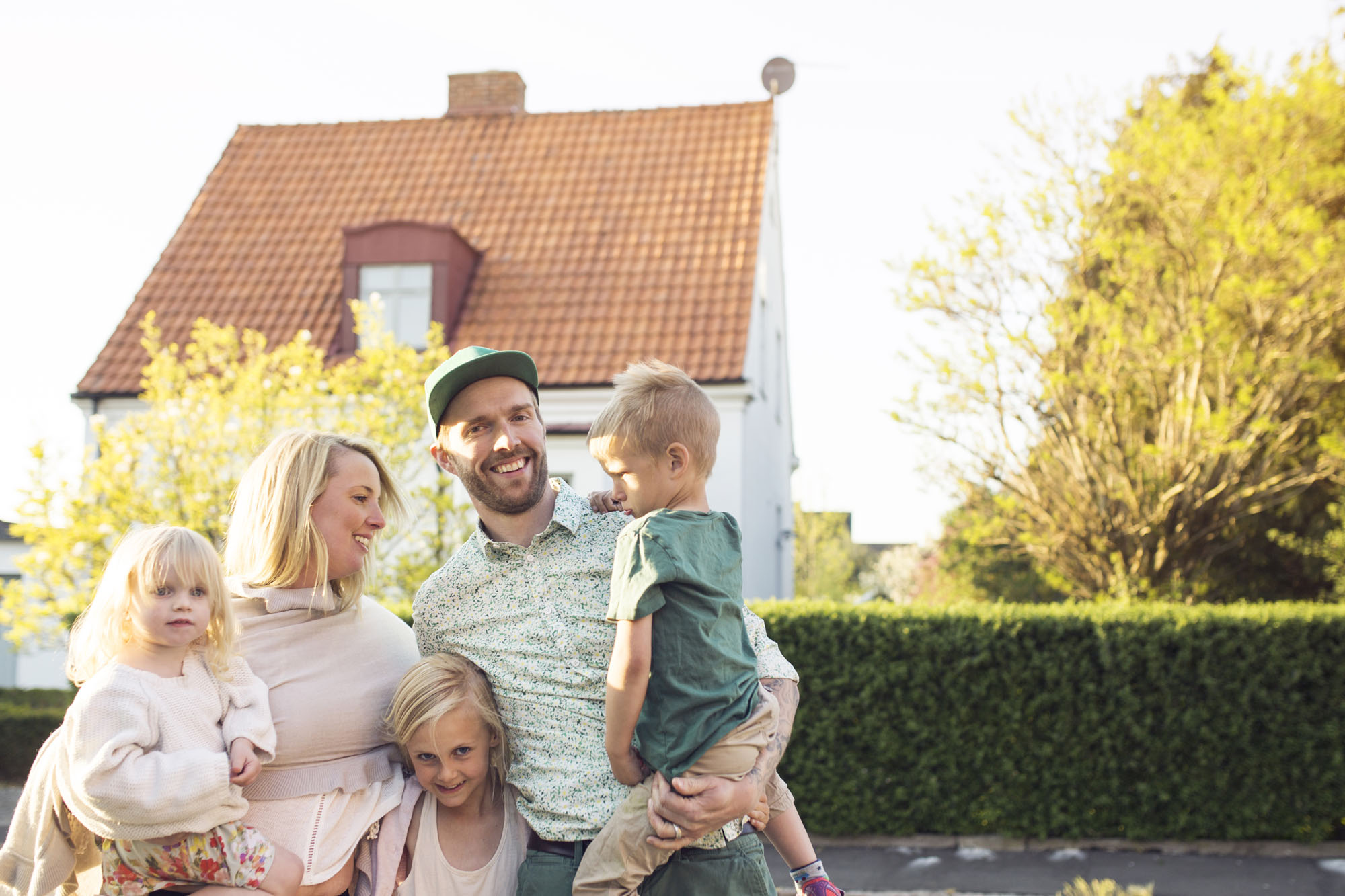 Family with children (18- 23 months, 4-5, 8-9 ) standing in in front of suburban house