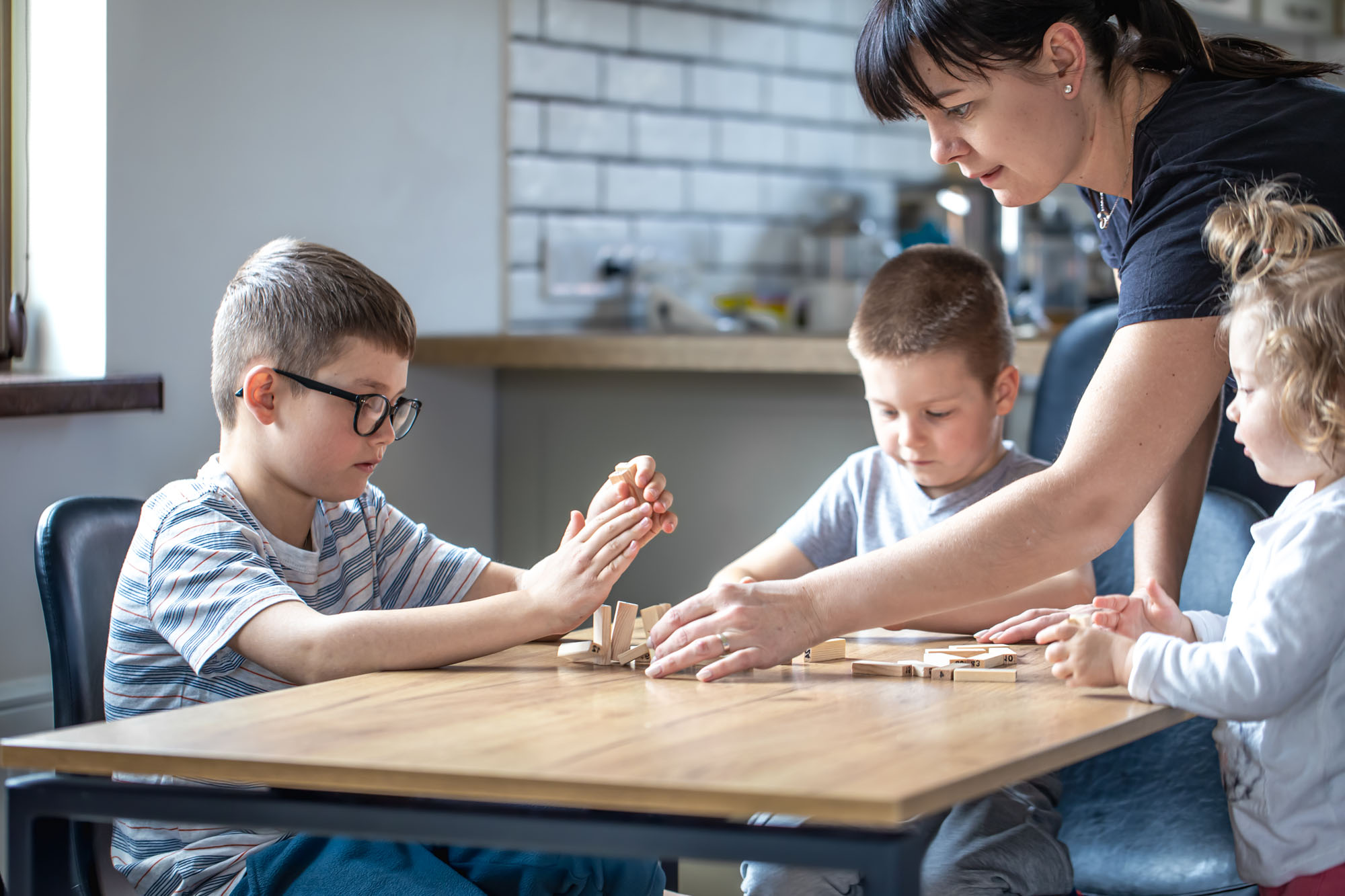 Children with their mother play board at home in the kitchen.