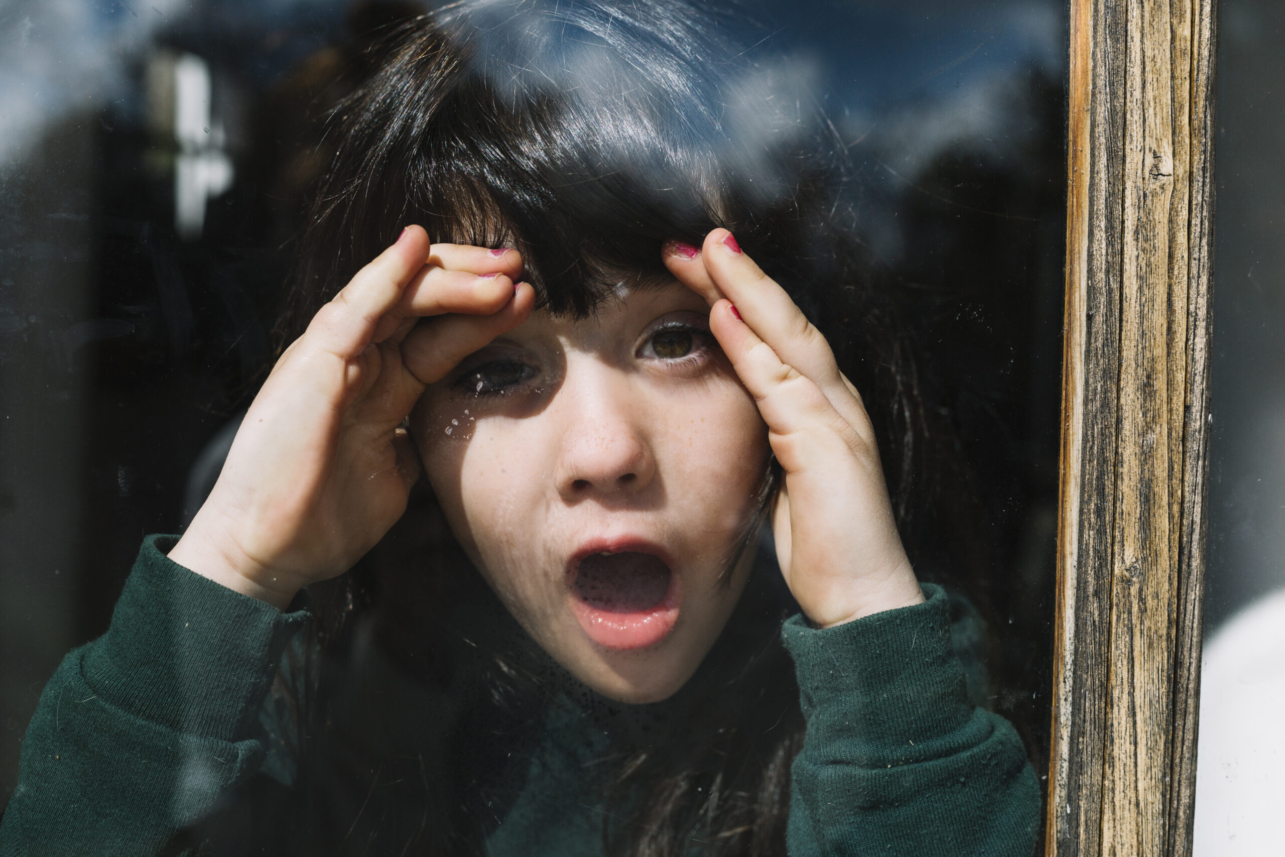 close-up-girl-peeking-through-glass-window