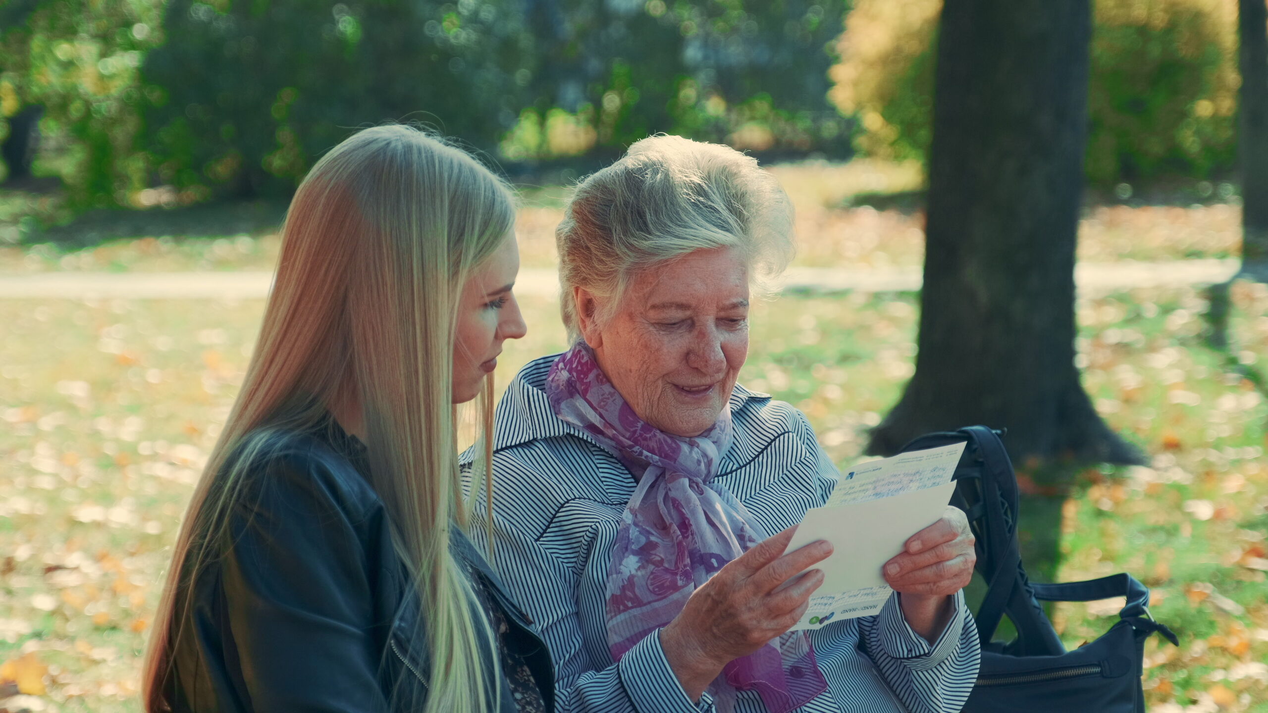 Middle close up of old woman reading a letter to pretty young woman in park
